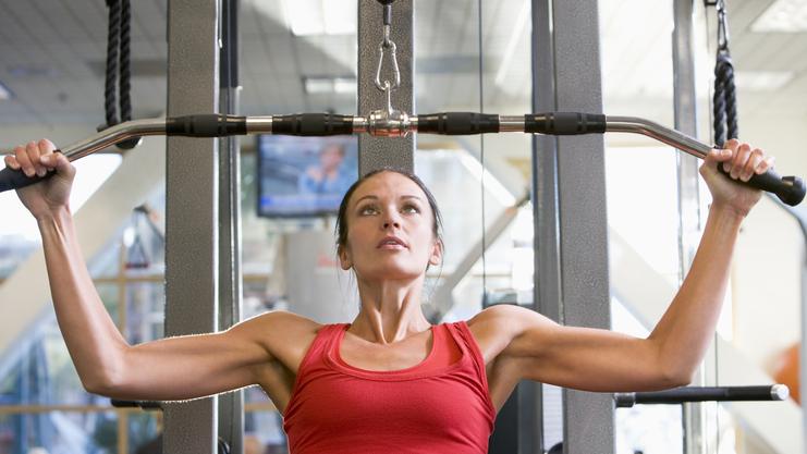 Frau in rotem Top trainiert an einer Kraftmaschine mit Latzuggriff im Fitnessstudio.