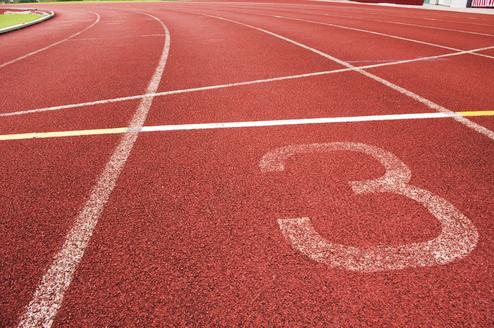 Nahaufnahme eines roten Laufbahnabschnitts mit der Markierung der Bahn 3 und weißen Linien.