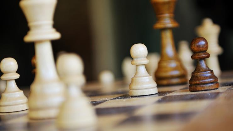 Nahaufnahme von Schachfiguren auf einem Schachbrett, mit weißen und dunkelbraunen Bauern in Fokus.